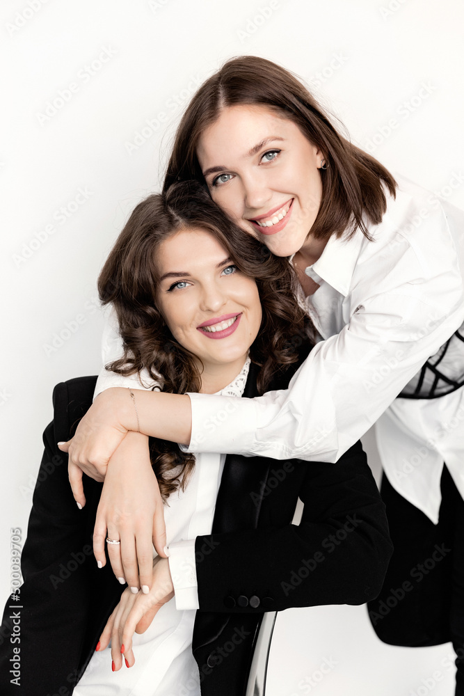Close up portrait stylish gorgeous ladies wearing luxury fashionable suit, look at the camera, smiling. Beautiful business women in formal wear sit on the chair at studio on white background Close up portrait stylish gorgeous ladies wearing luxury fashionable suit, look at the camera, smiling. Beautiful business women in formal wear sit on the chair at studio on white background