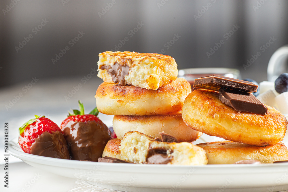 Cottage cheese pastries with strawberry, syrniki stuffed with chocolate on a white plate, selective focus