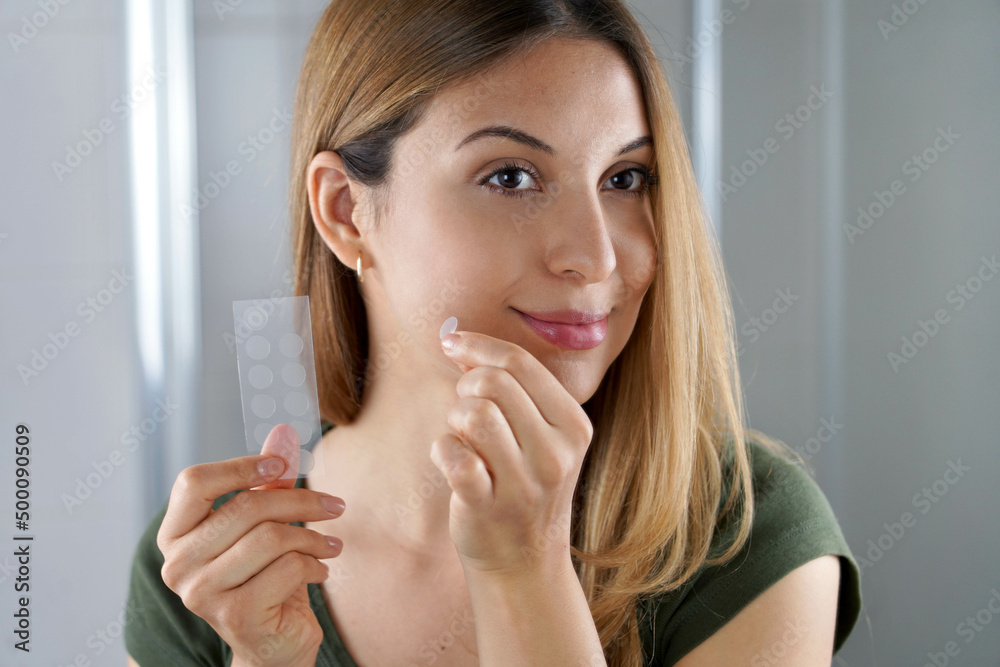 Beautiful young woman applying acne treatment anti-pickel patch on a pimple in bathroom at home Beautiful young woman applying acne treatment anti-pickel patch on a pimple in bathroom at home