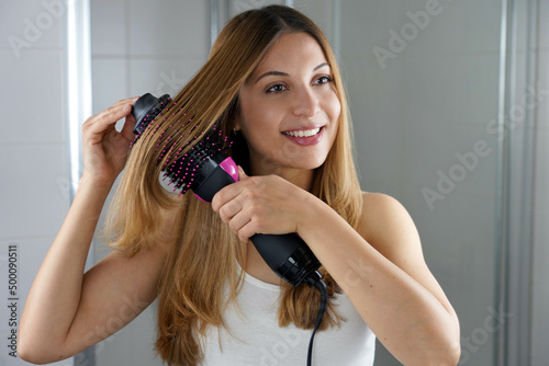 Young woman holds round brush hair dryer to style hair in an easy way at home