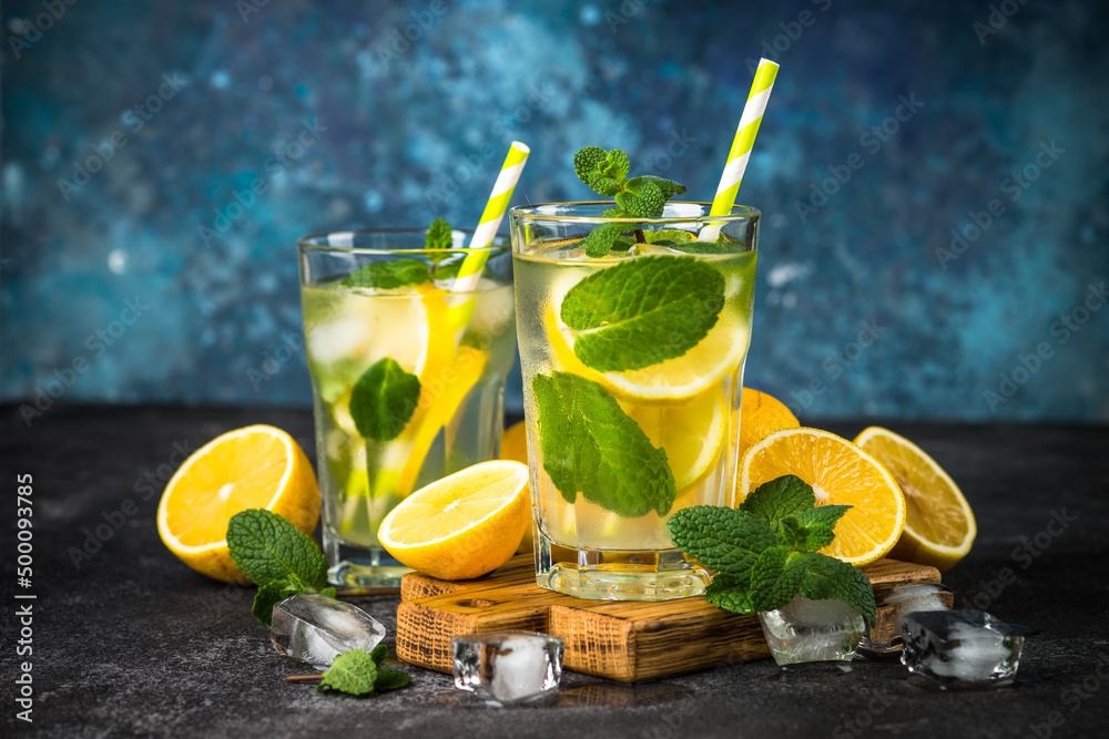 Fototapeta premium Lemonad in the glass. Traditional summer drink with lemon, mint and ice cube at dark table.