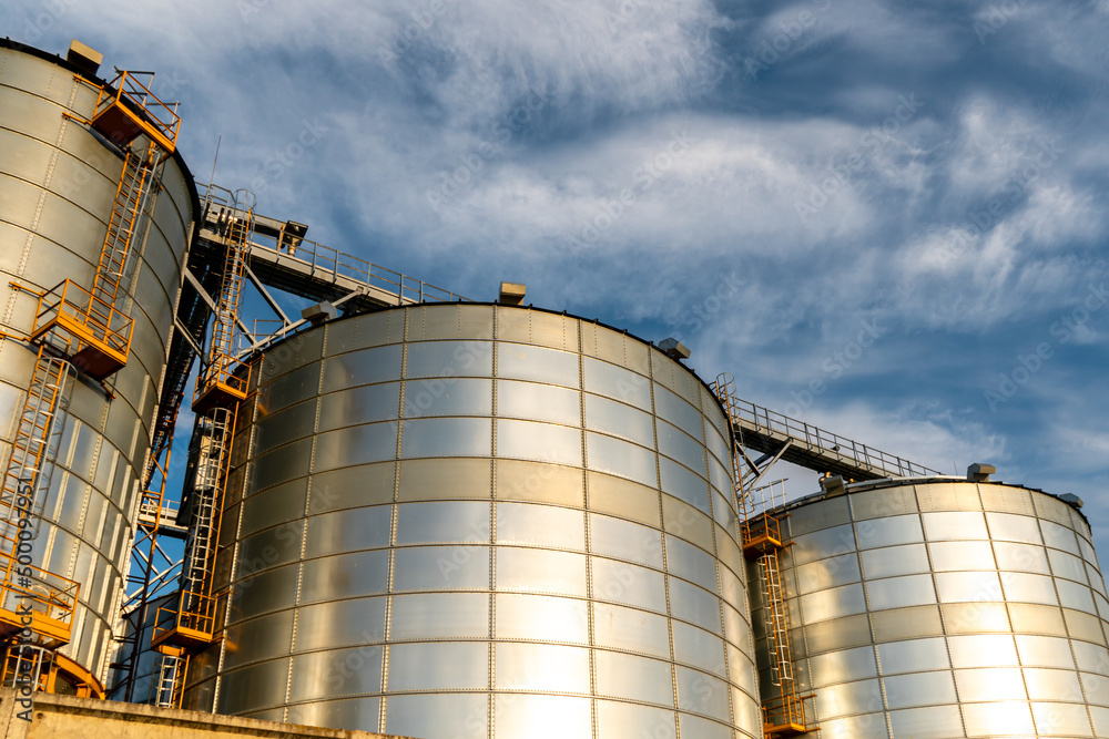 silver silos on agro manufacturing plant for processing drying cleaning and storage of agricultural products, flour, cereals and grain. Large iron barrels of grain. Granary elevator silver silos on agro manufacturing plant for processing drying cleaning and storage of agricultural products, flour, cereals and grain. Large iron barrels of grain. Granary elevator