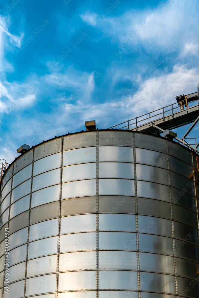 silver silos on agro manufacturing plant for processing drying cleaning and storage of agricultural products, flour, cereals and grain. Large iron barrels of grain. Granary elevator