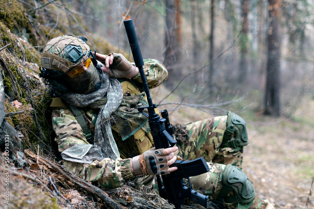 Special forces soldier during a clash in the forest. He calls his group's support on the walkie-talkie. Concept of modern military operations.