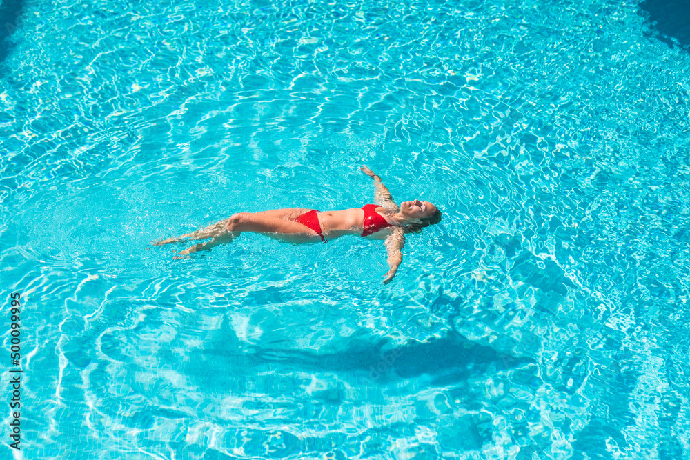 Beautiful adult woman floating on transparent water in swimming pool having relax and enjoying summer leisure water activity. Holiday vacation and happiness . Female people swim on blue sea surface
