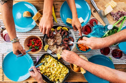 Vertical view of group of friends or family eating together. Friendship and celebration at lunch time with food. People enjoying meal taking from dishes. Concept of nutrition and social real life