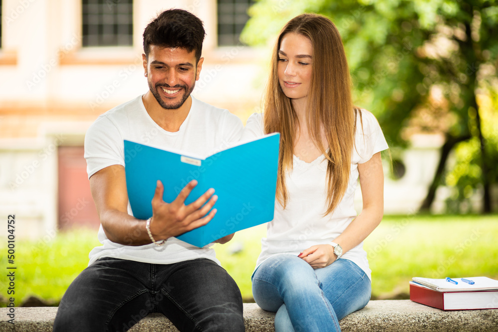 Fototapeta premium Two students studying together sitting on a bench outdoor