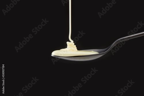 Cream or condensed milk pouring down in a black spoon against a black background. photo