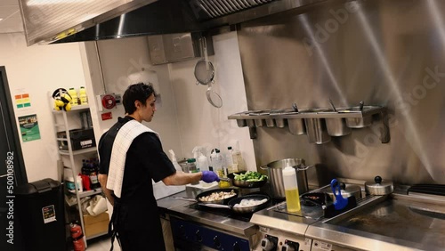 Professional chef in the kitchen of a restaurant. A male chef in a black uniform is working in the kitchen. Slow motion 4K