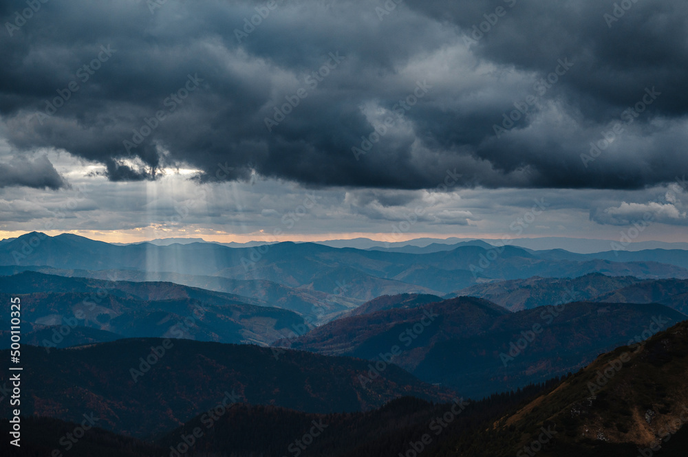 Sunbeams in dark clouds over tops of picturesque mountains Sunbeams in dark clouds over tops of picturesque mountains