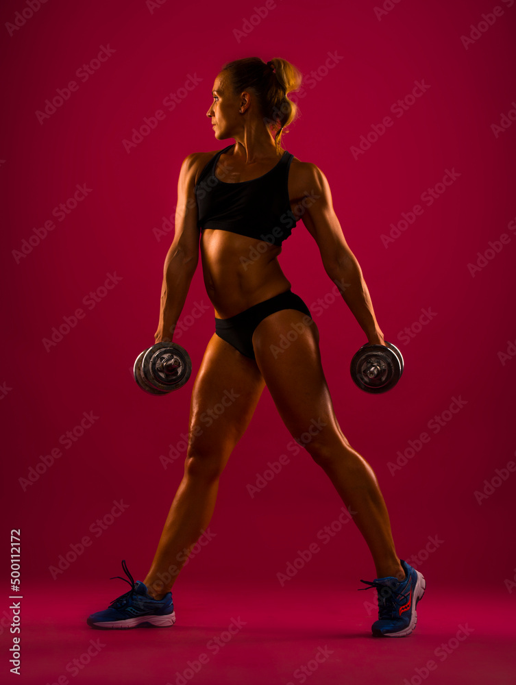 Athletic young woman doing a fitness workout with weights, isolated on red background 
