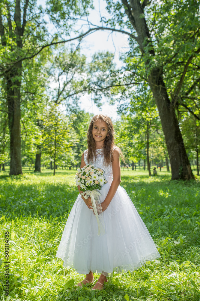 Little girl in a white dress with a bouquet of flowers in a summer park.