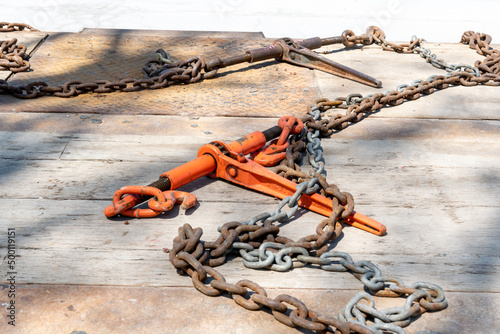 A ratchet load binder and tie down chain on the wooden deck of a flatbed truck tailer. photo