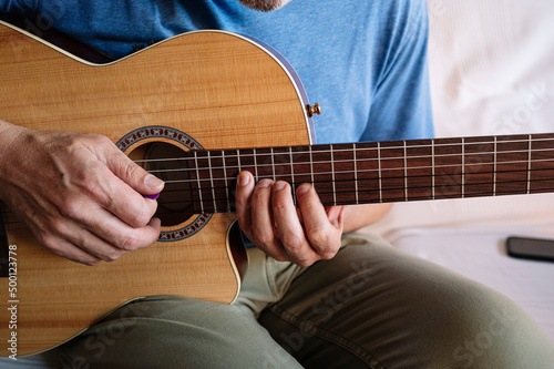 Adult man studying guitar online with tablet at home.