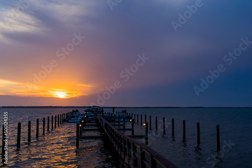 A purple sunset looking down a dock that has small lights. © Margaret Burlingham