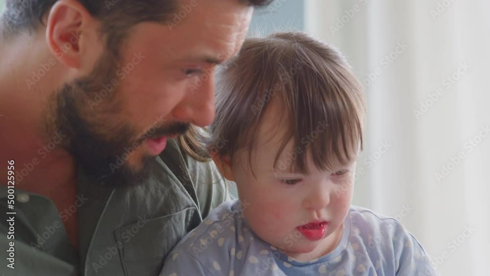 Close up of Down syndrome girl sitting with father at home reading book together - shot in slow motion Close up of Down syndrome girl sitting with father at home reading book together - shot in slow motion