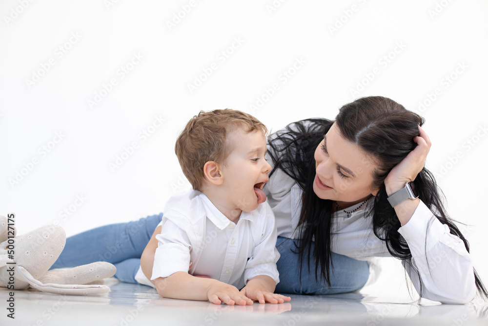 Black haired woman teacher and little boy showing tongue, lying on floor. Logopedics, early development, speech therapy Black haired woman teacher and little boy showing tongue, lying on floor. Logopedics, early development, speech therapy