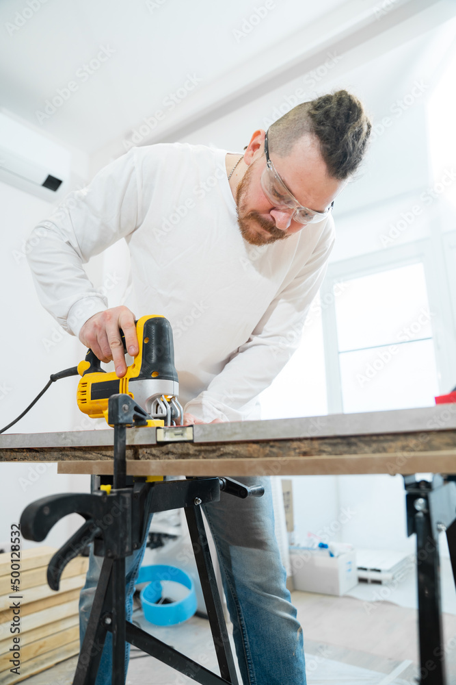 carpenter in protective glasses cuts wood with electric jigsaw carpenter in protective glasses cuts wood with electric jigsaw