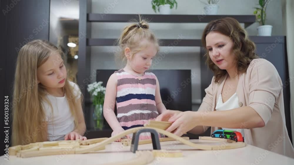 mom and daughters play with wooden toy railway. mom and daughters play with wooden toy railway.