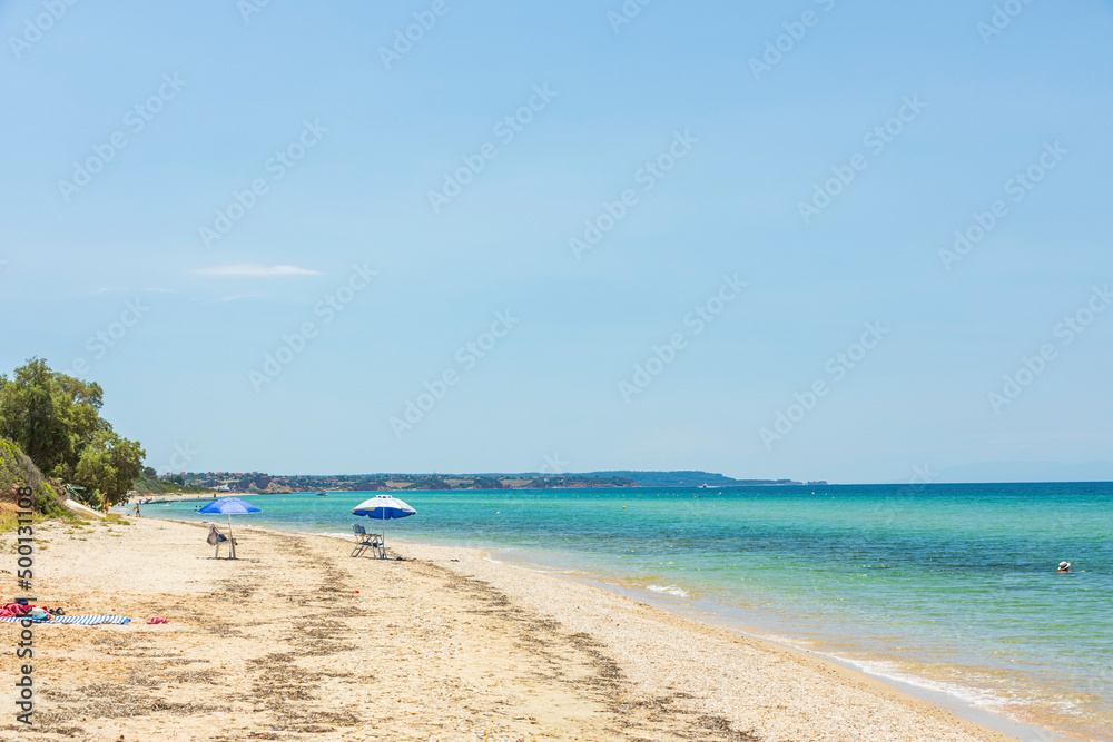 Beautiful seascape view. People on sand beach on turquoise water and blue sky background. Greece.