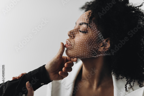 Creative photo. A man's hand holds the face of an african american woman with curly hair with a mesh on her face