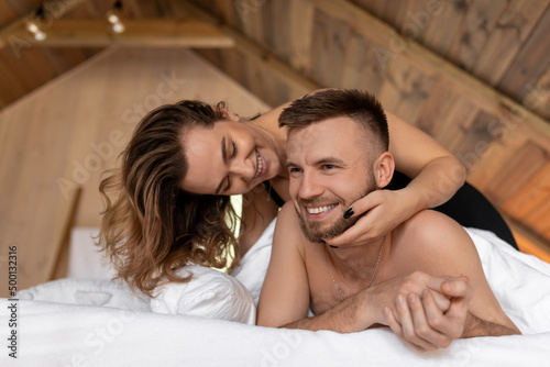 Portrait closeup from below of couple in love caressing, having fun and smiling on bed. Spend weekend at home and relax in cozy wooden bedroom. Love story, passion and feelings of young people