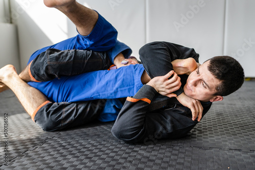 Two brazilian jiu jitsu BJJ athletes training at the academy martial arts ground fighting sparring wear kimono gi sport uniform on the tatami mats leg bar attack copy space