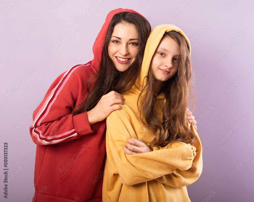 Happy smiling beautiful young mother and cute daughter hugging in fashion trendy hoodie together on purple studio background with empty copy space. Happy loving family