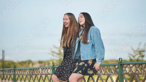 Two girlfriends talking sitting on the fence. photo