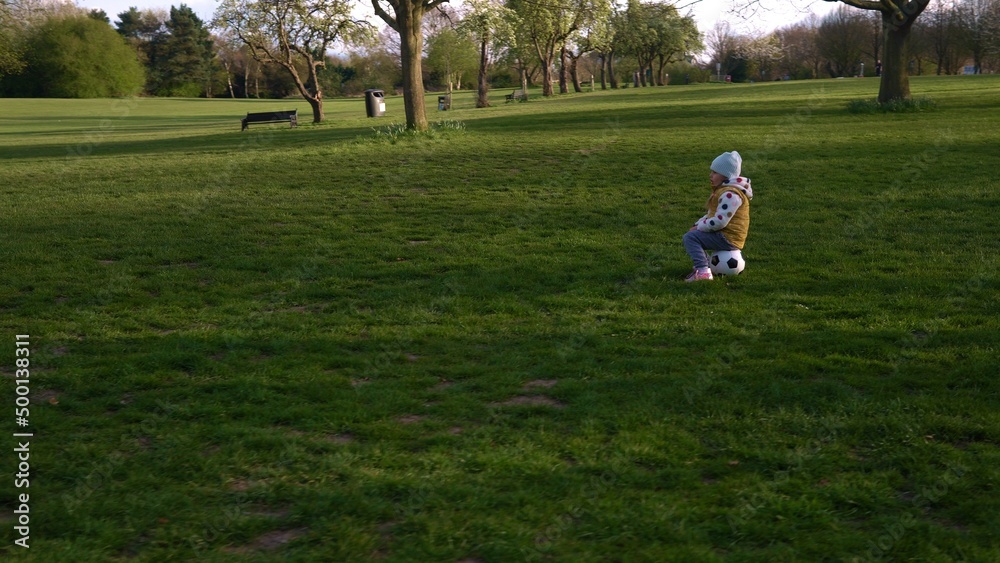Happy Family Of Children Having Fun In Spring Park. Little Kid Run. Child Girl Dribbles Black White Classic Soccer Ball On Green Grass. People Playing Football. Childhood, Sport, Championship Concept Happy Family Of Children Having Fun In Spring Park. Little Kid Run. Child Girl Dribbles Black White Classic Soccer Ball On Green Grass. People Playing Football. Childhood, Sport, Championship Concept
