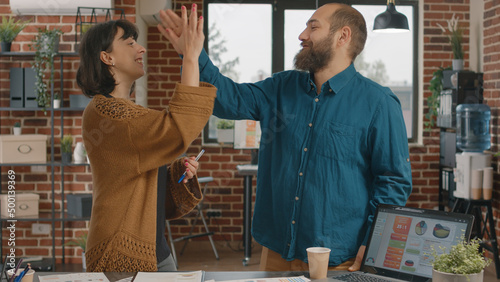 Colleagues giving highfive while brainstorming ideas to design project and plan marketing strategy. Man and woman celebrating success at research meeting, showing unity in startup office. photo