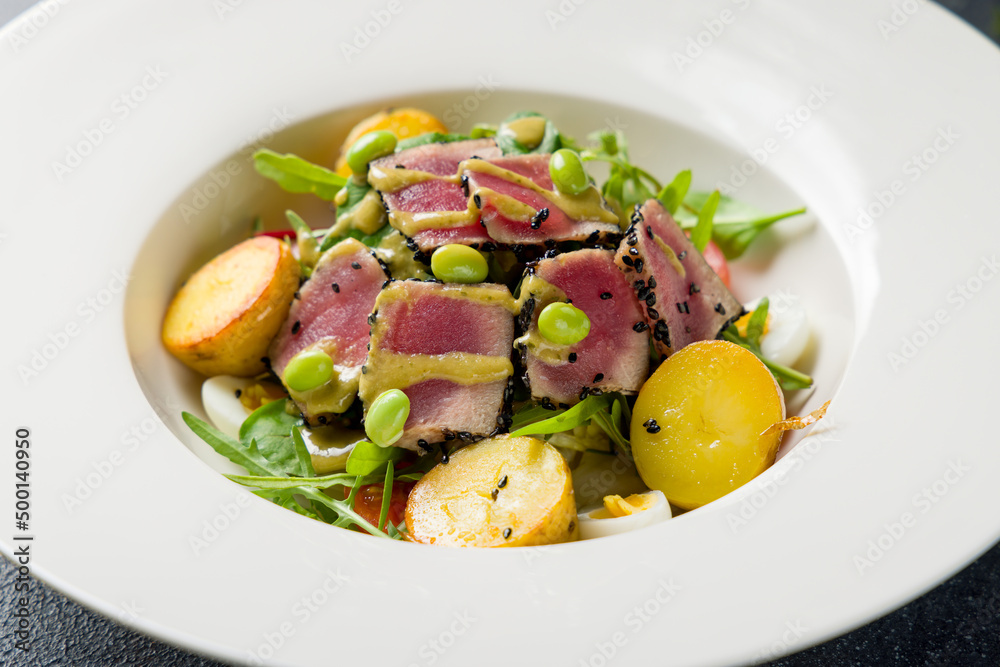 Nicoise with tuna and baby potatoes on white plate on dark stone table macro close up Nicoise with tuna and baby potatoes on white plate on dark stone table macro close up