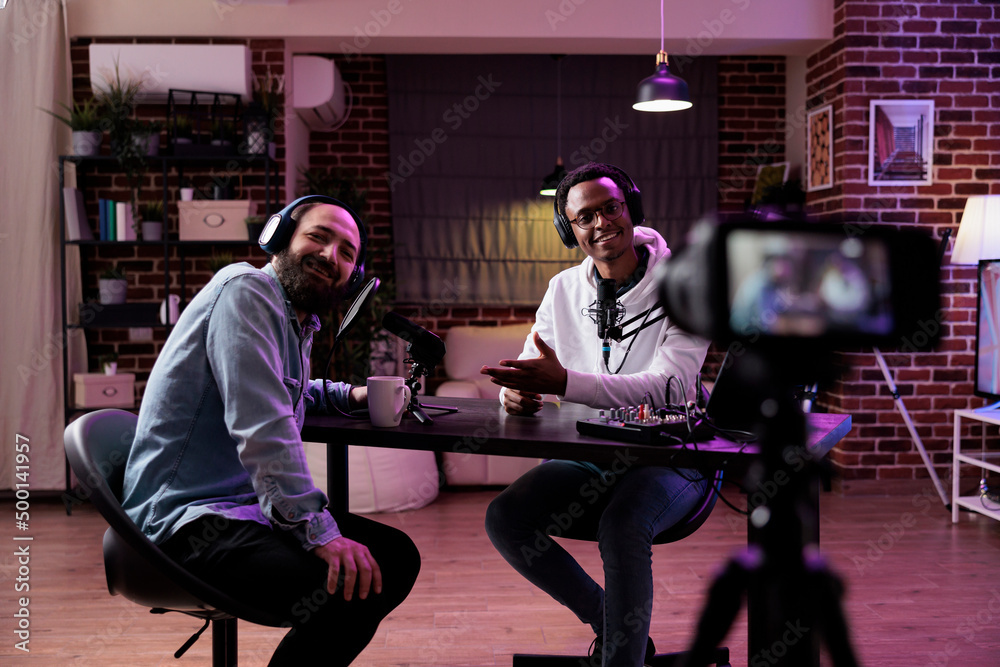 Male influencer using camera to record podcast conversation, filming talking show discussion in studio. Social media vlogger chatting and broadcasting live, meeting with happy guest. Male influencer using camera to record podcast conversation, filming talking show discussion in studio. Social media vlogger chatting and broadcasting live, meeting with happy guest.