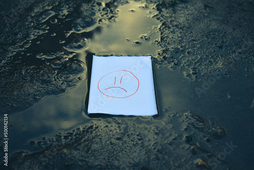 white paper with sad face drawing lying in a puddle