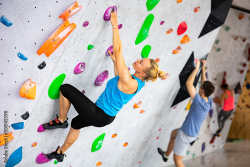 Woman climbing a tall, indoor, man-made rock climbing wall
