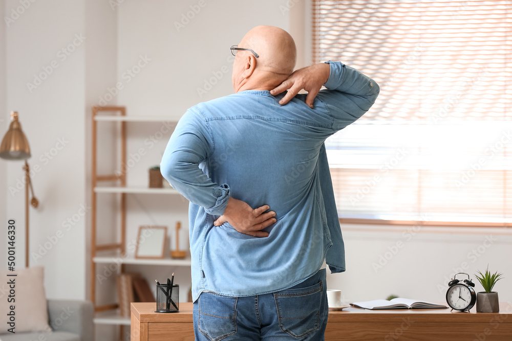 Senior man suffering from back pain near table at home Senior man suffering from back pain near table at home