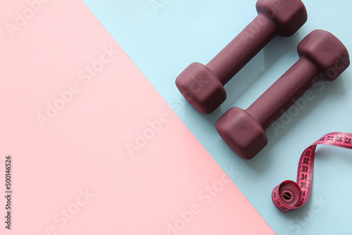 Stylish dumbbells and measuring tape on color background