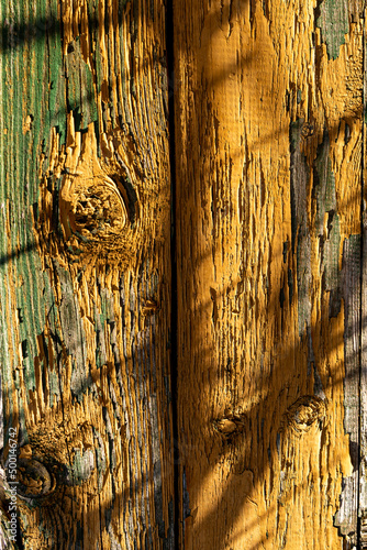 Yellow wodden planks covered with old flaking paint and visible wood patches, aged wodden wall surface with shades cested on it making a good background material photo