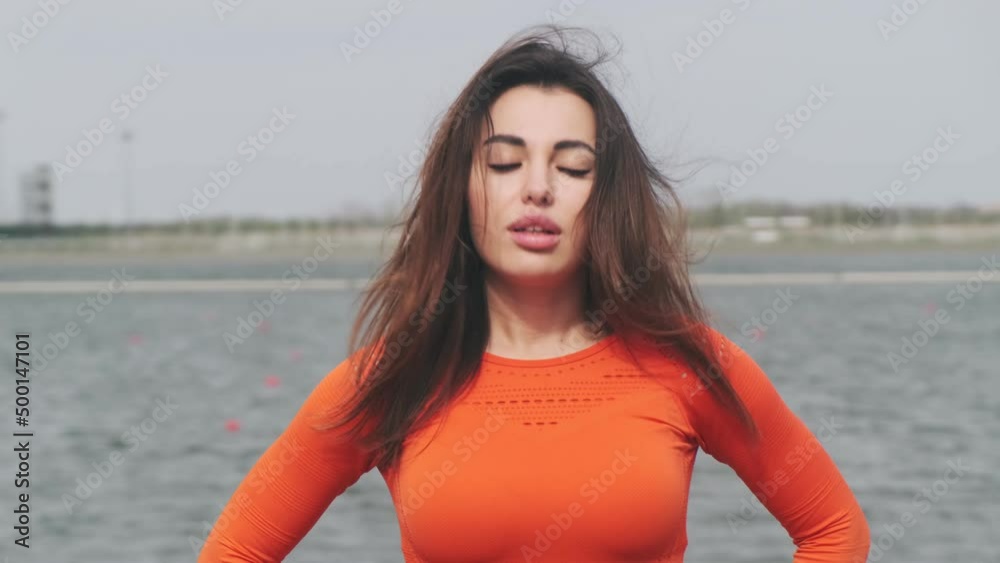 Beautiful athletic woman doing head tilts, stretching her body, warming up before training outdoors. Girl in sportswear exercising outdoors for health and wellness. Slow motion
