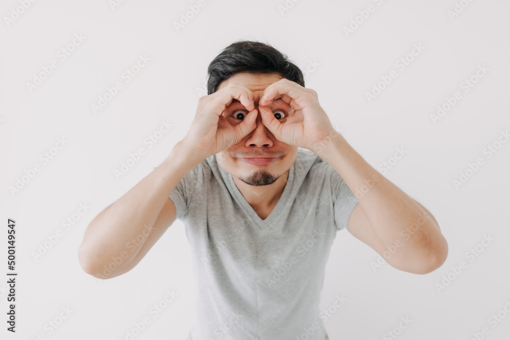 Funny obvious peeking Asian man in grey t-shirt isolated on white background. Funny obvious peeking Asian man in grey t-shirt isolated on white background.