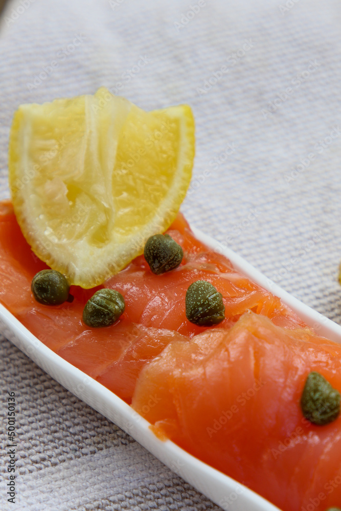 Fresh smoked salmon and capers with lemon on a white plate.