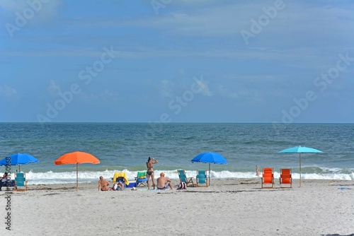 Fototapeta Naklejka Na Ścianę i Meble -  Tourists and locals enjoying a warm sunny day at the beach with umbrellas and chairs on Cocoa Beach, Florida near Cape Canaveral. 