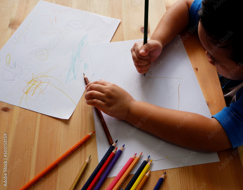 Cute Asian boy drawing with color pencils and white paper on wooden table Cute Asian boy drawing with color pencils and white paper on wooden table