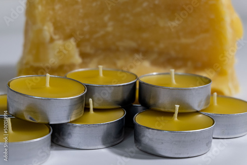 Bulk beeswax tealights are displayed in front of a raw beeswax block. photo