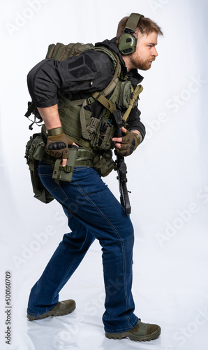 airsoft player in full gear is ready to play. a man in an outfit, in headphones, a bulletproof vest, with a backpack and a belt with additional shells. on a white background.
