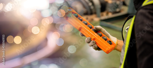 Worker man hand push remote control switch for overhead crane in factory, technician operating controlling the lift at factory industrial warehouse