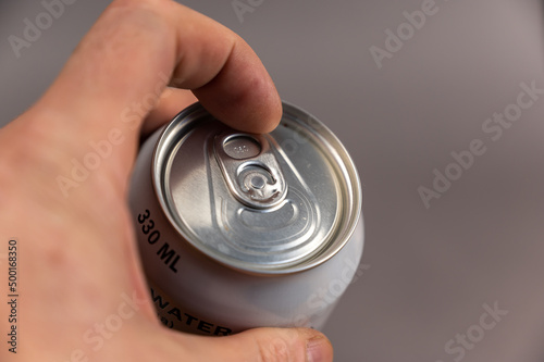 A man is holding a can of drink in his hand. A silver metal can of beer, soft drink, or water. Close-up, selective focus.