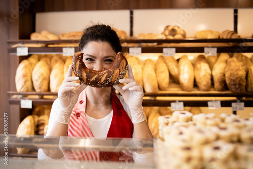 Portrait of bakery seller making funny smiling face with croissant in bakery shop.