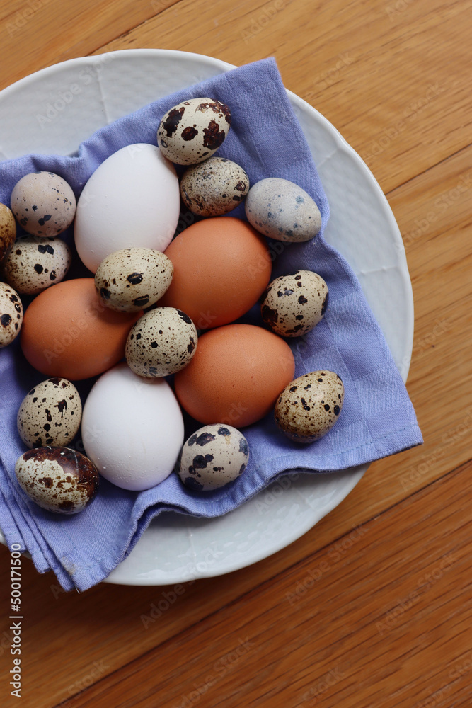 Fresh chicken brown and white eggs and quail eggs in a bowl on wooden table Fresh chicken brown and white eggs and quail eggs in a bowl on wooden table