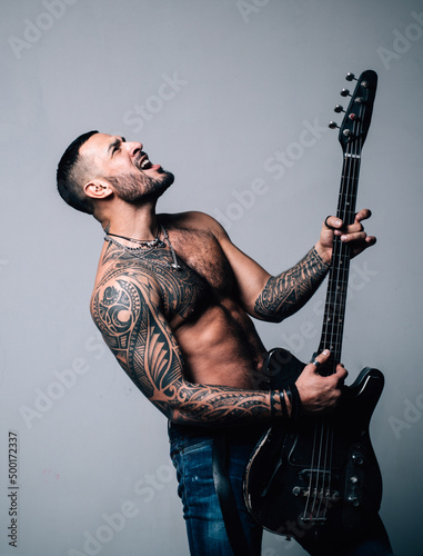 Expressive young man playing rock-n-roll music on electric guitar. Excited sexy man with electric guitar. Instrument on stage and band. Strong, muscular, muscles guy. Music concept. Man playing guitar